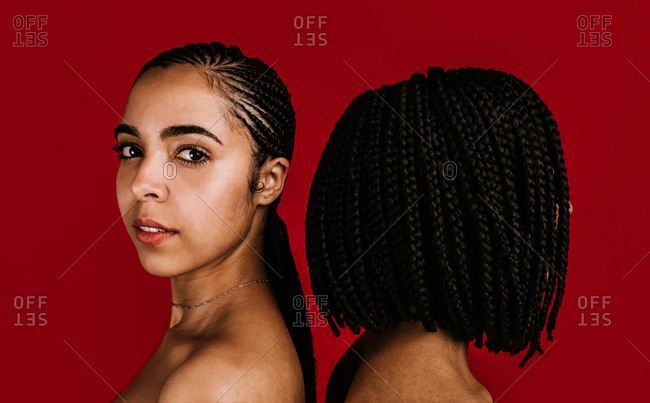A close up shot of two Black women standing back to back with long and short braided hair