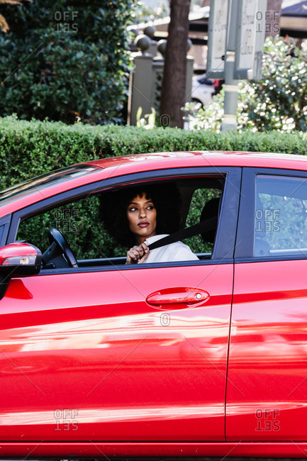 Vertical shot of a woman putting on the seat belt in a red car