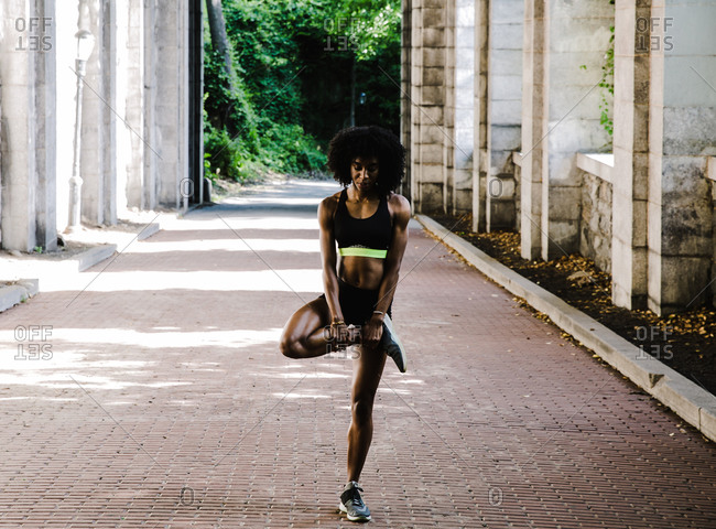 Black woman in athletic apparel performing a stretching exercise outdoors
