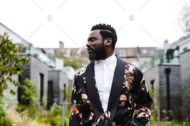 A medium shot of a black man looking sideways wearing a colorful flowery jacket