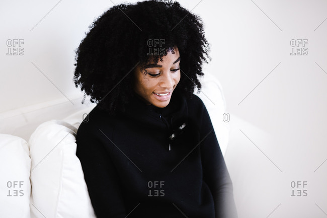 Portrait of a black woman sitting on white couch in a sweatshirt