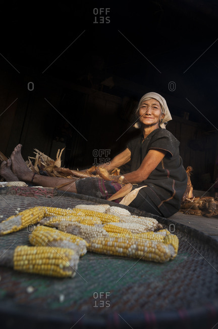 An Akhu woman sits behind a tray of corn