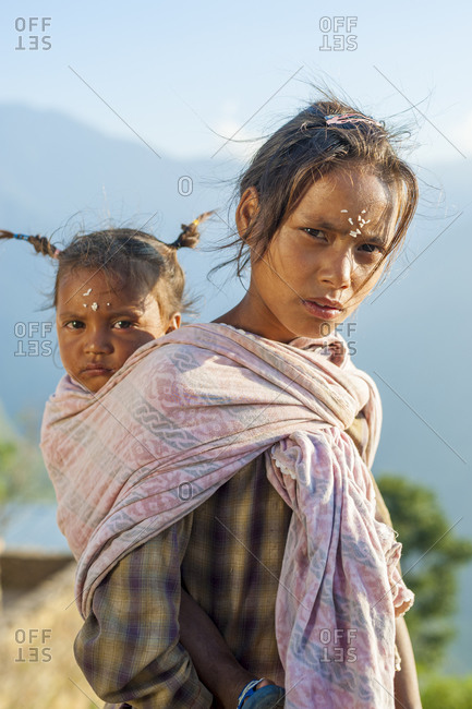 A little girl carries a baby in a rural village in western Nepal