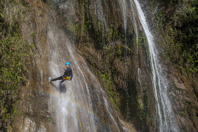 A girl gets soaked under a waterfall as she rappels down a rope canyoning in Nepal