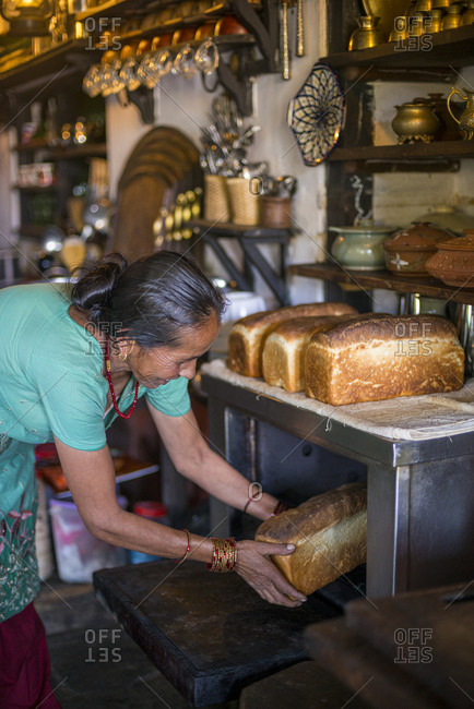 Baker taking out freshly baked bread from the oven of a bakery stock photo