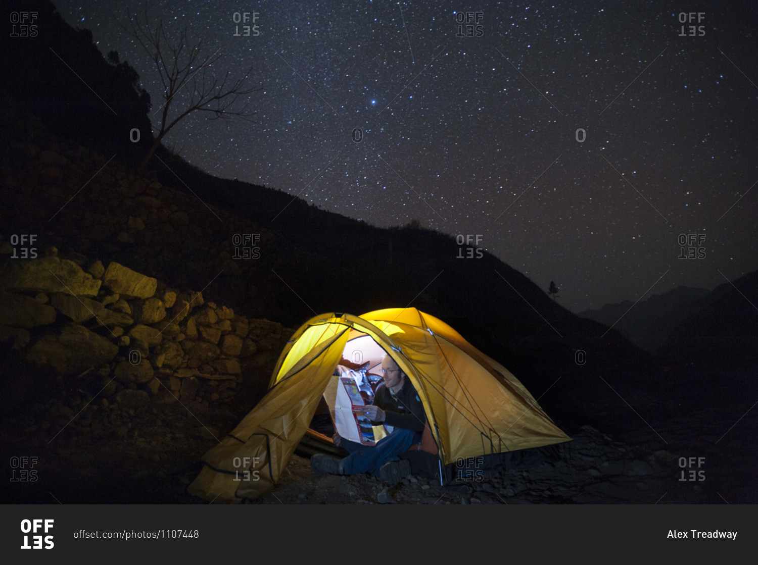 A man reads a map by torchlight inside his tent in the Manaslu region