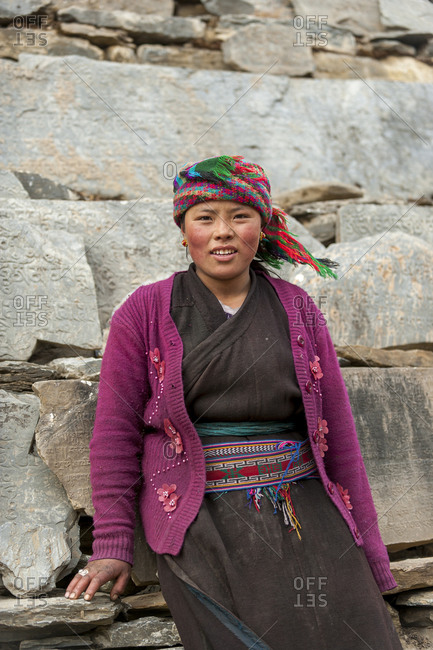 A Tibetan girl in the Tsum valley stands next to a wall of Mani stones