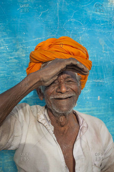 a farmer from Bundi wearing a bright orange turban sitting in front of a vibrant blue painted wall which is a typical sight in Rajastan