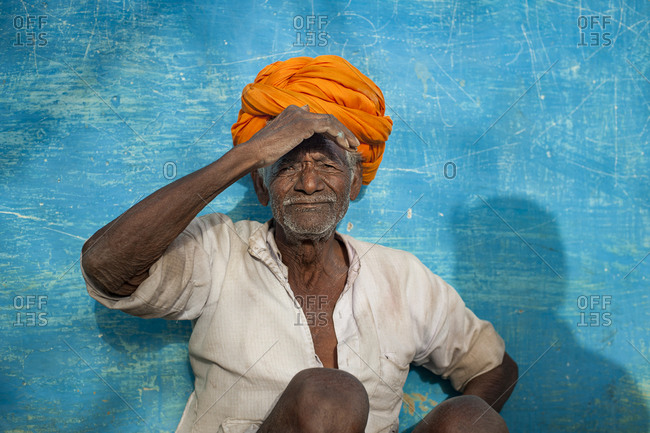 a farmer from Bundi wearing a bright orange turban sitting in front of a vibrant blue painted wall which is a typical sight in Rajastan