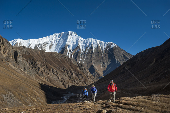 Trekkers walk up the Kagmara valley in Dolpa, a remote region of Nepal, with views of Lhashama in the distance