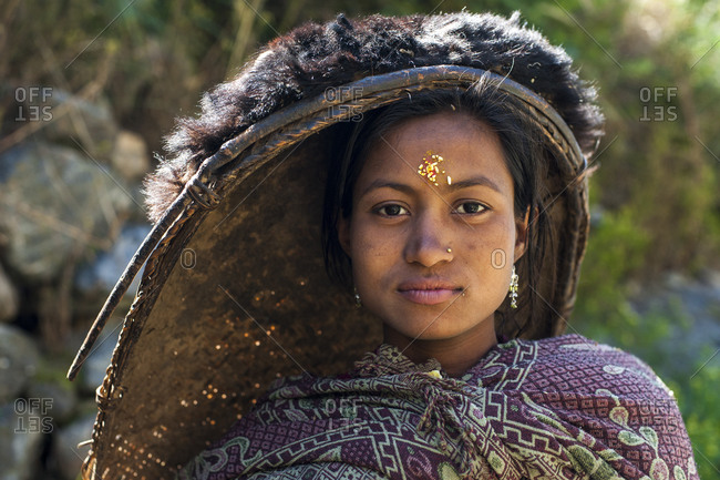 A woman from Dolpa wearing traditional clothes and carrying a bamboo rice pan for winnowing rice on her head