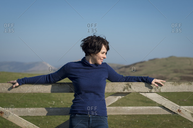 A perfect sunny day in Dorset on the south coast of England. A woman looks out to sea while taking a rest on a gate