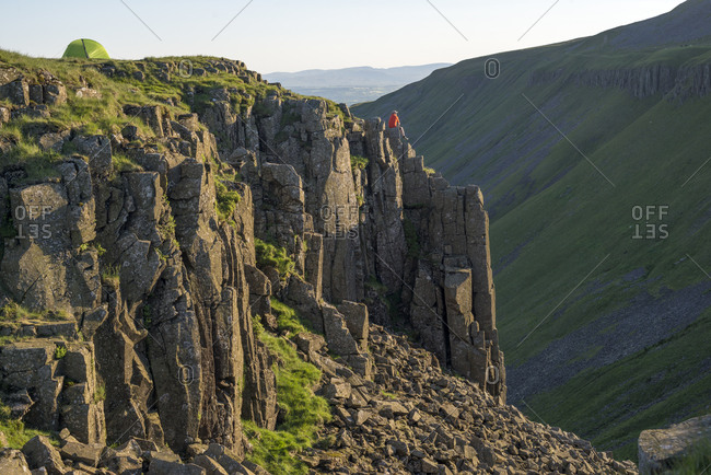 A man hiking the Pennine Way sits on the edge of the huge escarpment in the Yorkshire Dales called Highcup Nick