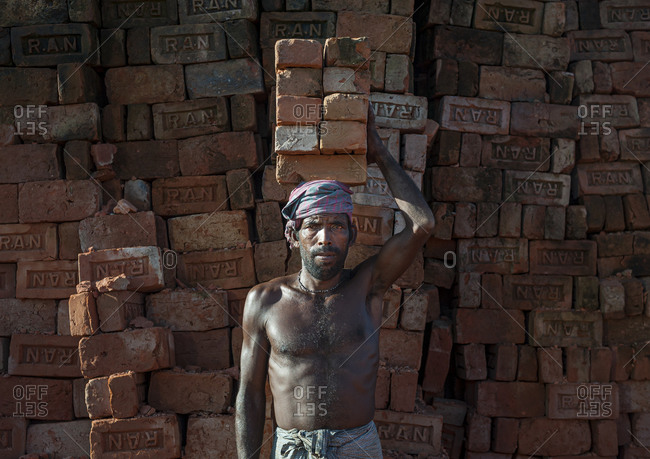 A man laboring in a brick factory will carry up to 50 Kilos of bricks by balancing them on his head