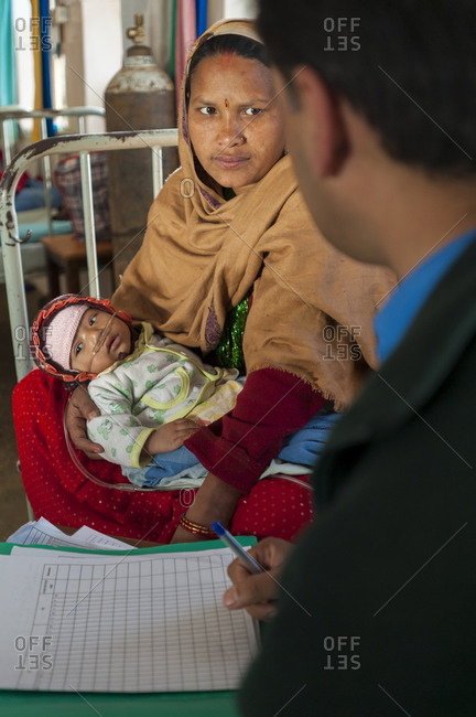 Tansen, Palpa district, Nepal - August 1, 2010: A woman holds her baby while being consulted by a doctor at Tansen Hospital