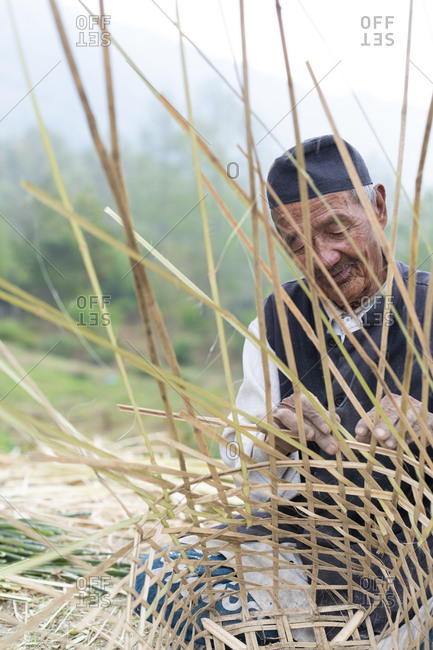 A old Nepali man makes a traditional basket called a Doko by weaving bamboo