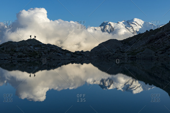 Hikers and the summit of Mont Blanc reflected in Lac Blanc on the Tour du Mont Blanc trekking route in the French Alps