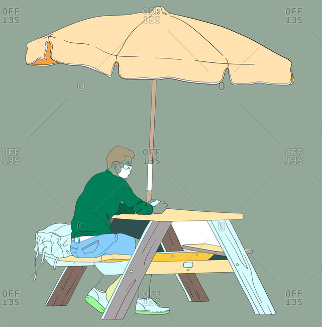Young man wearing a mask and waiting at a wooden table under an umbrella at the beach