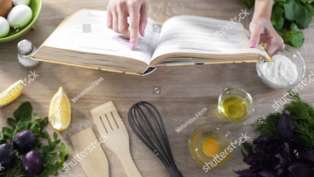 Lady reading pizza recipe in culinary book at home with kitchenware on table