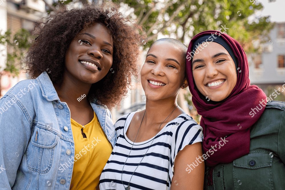 Grupo de tres felices amigos multiétnicos mirando las cámaras. Retrato de mujeres jóvenes de diferentes culturas disfrutando de vacaciones juntas. Chica islámica sonriente con dos amigos afroamericanos al aire libre.