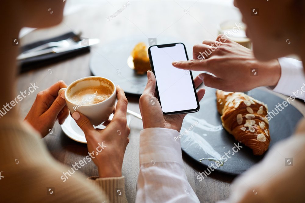 One of young contemporary females pointing at touchscreen of smartphone over table while having coffee with her colleague