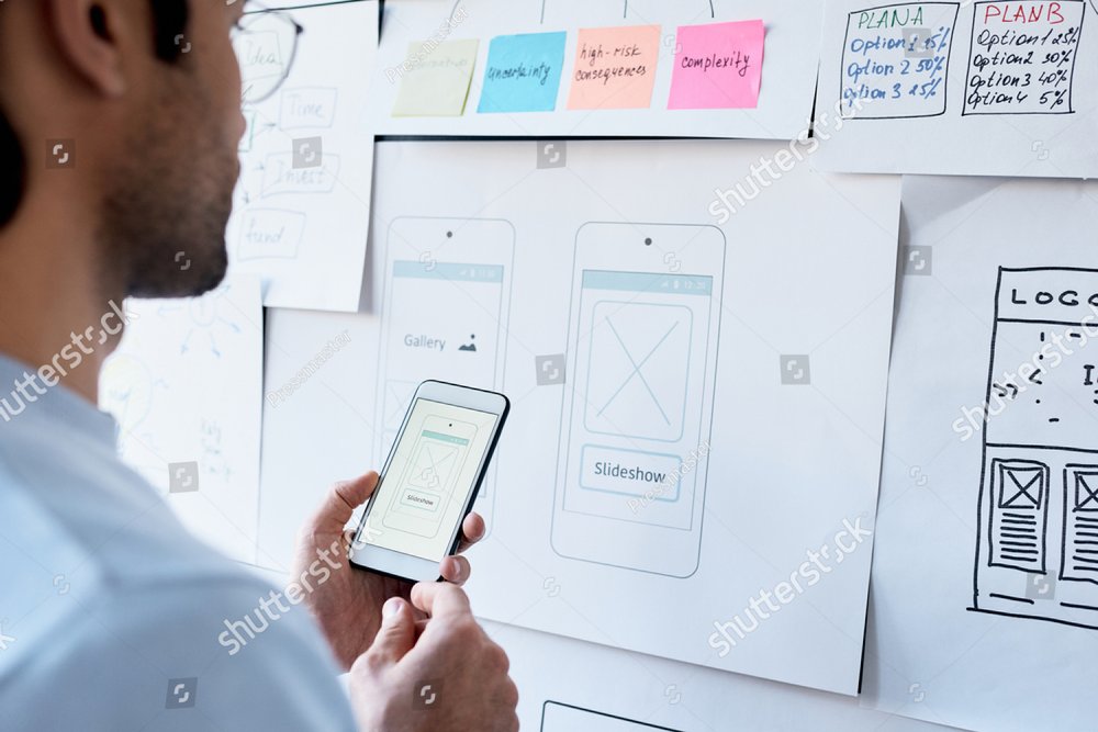 Over shoulder view of man using smartphone while designing slideshow effect in office with task board