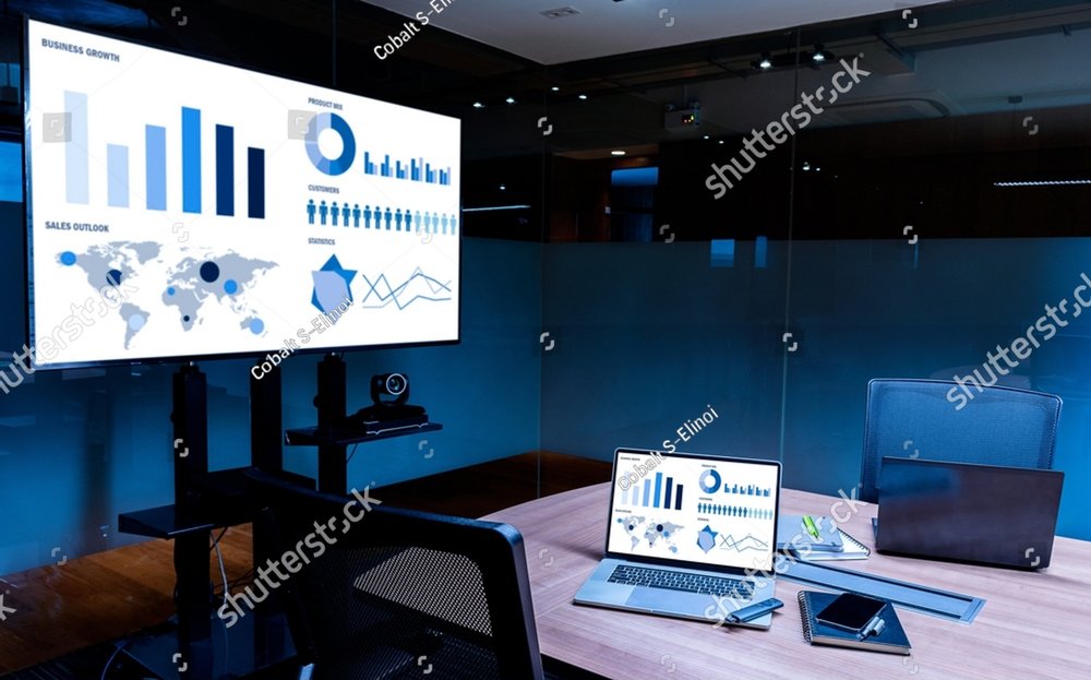 Mock up sales summary slide show presentation on display television and laptop with notebook on table in meeting room