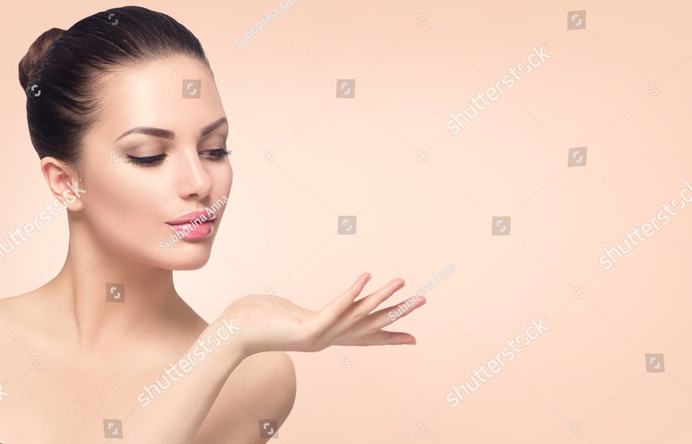 Beauty Spa Woman with perfect skin Portrait. Beautiful Brunette Spa Girl showing empty copy space on the open hand palm for text. Proposing a product. Gestures for advertisement. Beige background