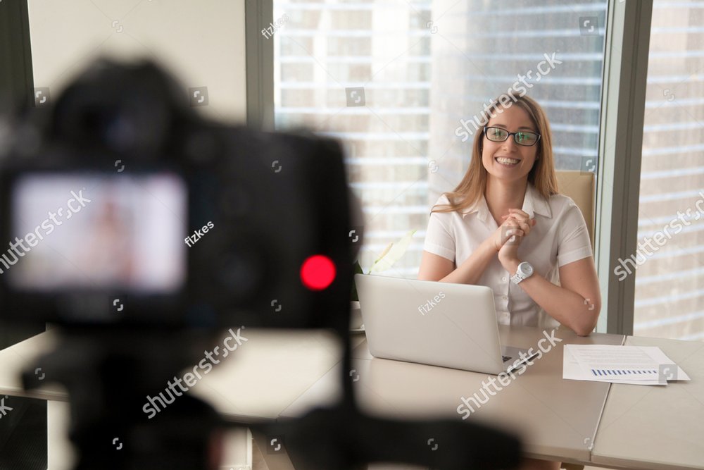 Smiling businesswoman talking on camera, happy entrepreneur vlogger recording business vlog at office desk for videoblog, filming promo ad, making presentation to website, video marketing production