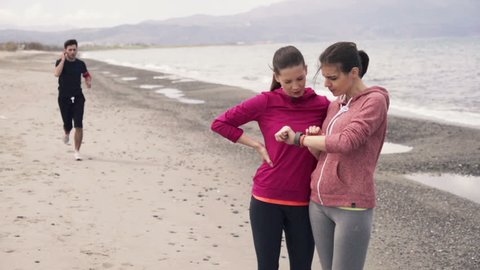 Sporty girlfriends with smartwatch on beach
