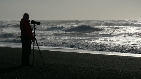 Waves breaking at the black sand beach of Reynisfjara southern coast of Iceland with a photographer in the defocused foreground