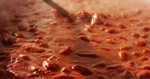 Slow motion of mixing hot Italian tomato sauce (passata) with a metallic spoon in a pan (macro close up)
