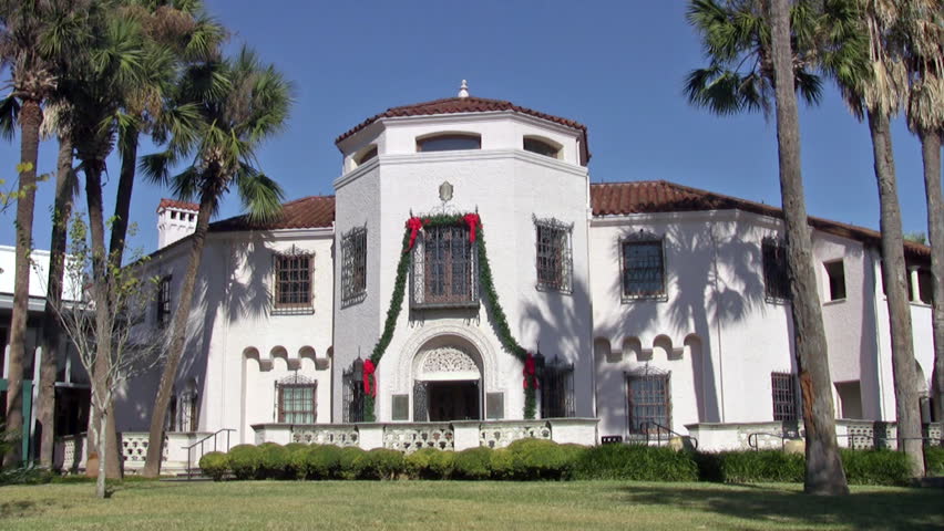 Video of the front entrance to the McNay Art Museum in San Antonio Texas. White stucco building with plush garden park. Palm trees, ponds and fountains.