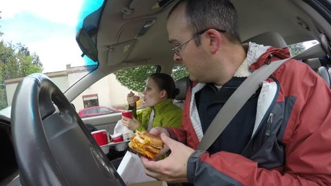 A family pulls pulls over in the car to eat their fast food hamburgers and french fries