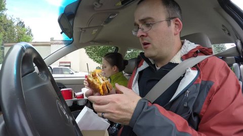 A time-lapse of a family eating fast food hamburgers and french fries while sitting in the car traveling