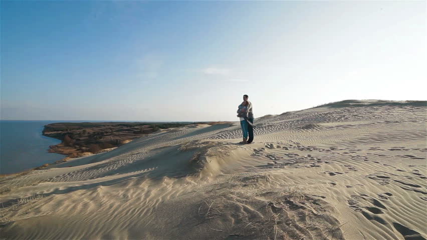 Beautiful flycam shot of young embracing couple standing on the top of enchanting natural sand dune hill and enjoying view to the sea