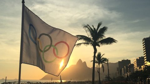 RIO DE JANEIRO, BRAZIL - FEBRUARY 12, 2015: An Olympic flag flutters in the wind in front of the sunset skyline at Ipanema Beach.