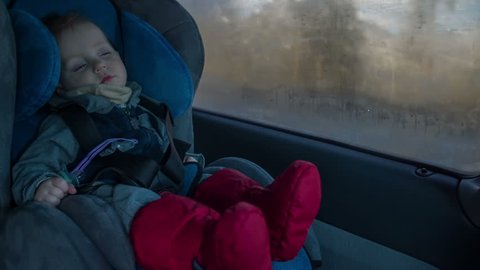 Cute boy sit in car chair. While driving on a high way the cut baby boy is slipping inn the chair on a sunny winter day footage in slow motion.