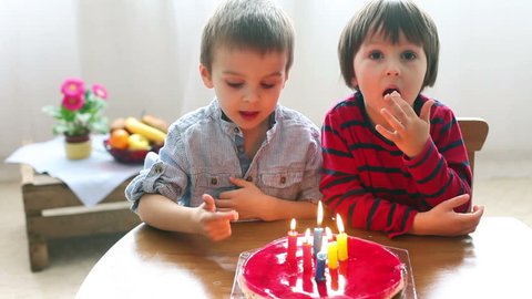 Adorable cute boys, blowing candles on a birthday cake at home