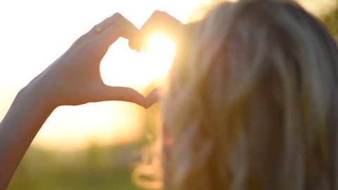 Beauty girl making heart with her hands over nature sunset background. Happy young woman. Silhouette hand in heart shape with sun inside. Vacation concept. Summer holidays. Slow motion 240 fps 1080p 
