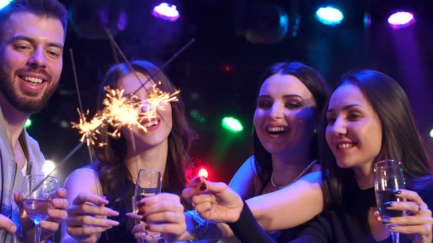 Portrait of four cheerful friends with champagne and sparklers on a background of flashing lights. | Shutterstock HD Video #1005609445