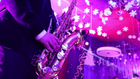 a male saxophonist with a musical band playing on stage in a restaurant, a saxophonist playing against a silhouette of dancing people, shallow depth of field
