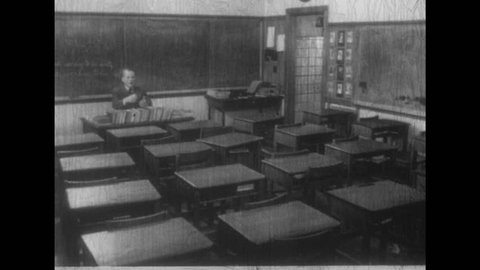 1950s: Man sits at head of empty classroom. Man packs briefcase. Man passes out papers to students at desks.