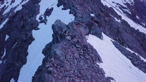 A smooth drone shot of rocky parts of a mountain covered in snow at sunset, filmed in New Zealand. 