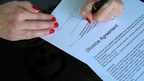 A woman signs a divorce agreement and takes off her wedding ring symbolically. Names and address fictitious.