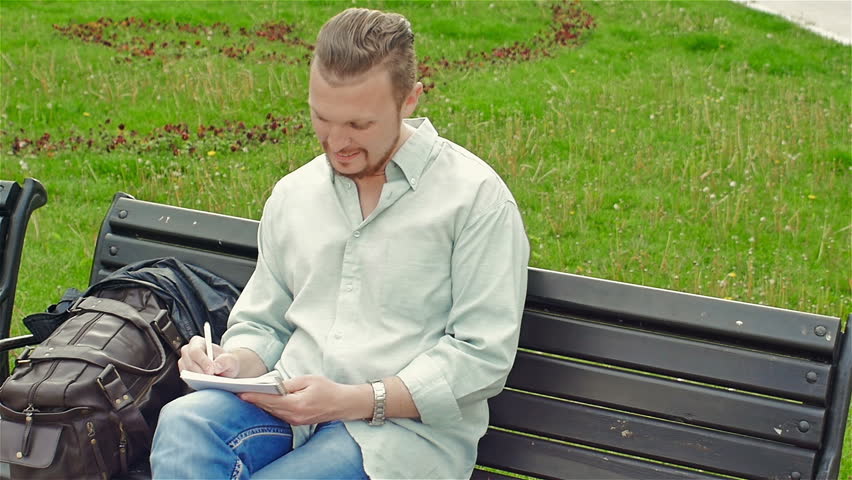 Adult, attractive man sitting on a bench making entries in the notebook