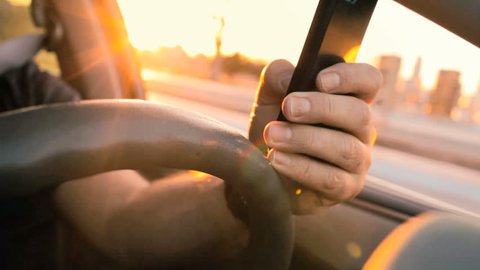 Texting while driving at sunset, distracted driver on cell phone 