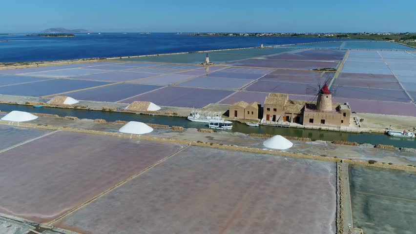 Aerial of salt pans showing different colored pans old windmill and tourist boat moving past the decomissioned salt windmill part of the Riserva Naturale Saline Di Trapani salt museum 4k quality Royalty-Free Stock Footage #1006567192