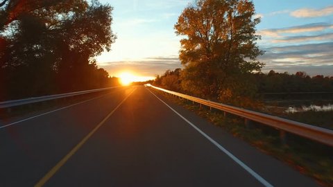 Driving a car on an empty and curvy Road at Sunset, low sun is shining brightly into the lens. Thousand Islands Parkway, Canada.A Gyro-stabilized camera was mounted on the hood of the car.
