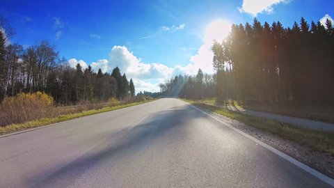 Beautiful countryside POV vehicle drive, asphalt road, trees, gleaming sun blue sky, car travel gopro point of view, sunny winter day 
